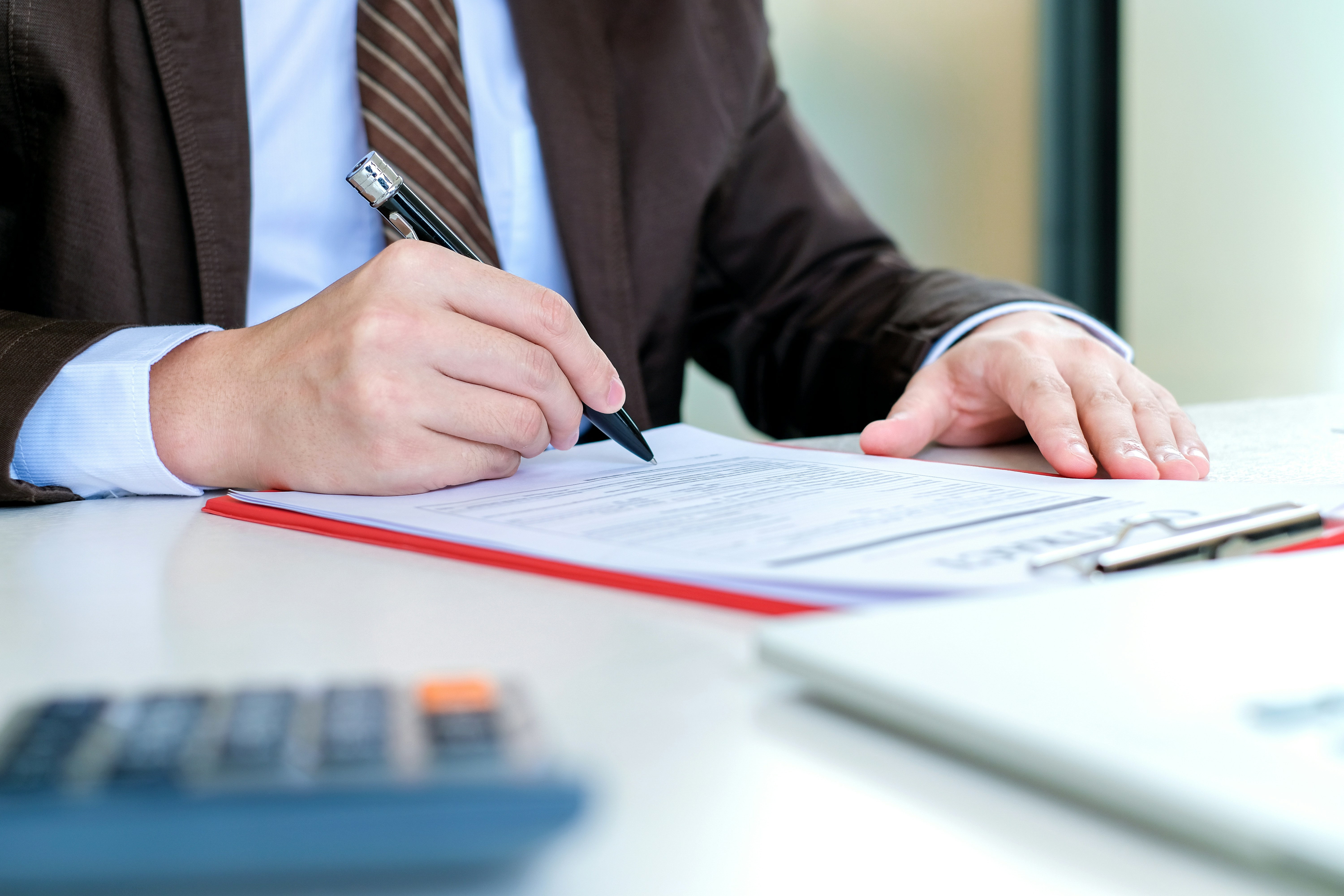 Person im Anzug unterzeichnet Dokument auf Klemmbrett mit Kugelschreiber